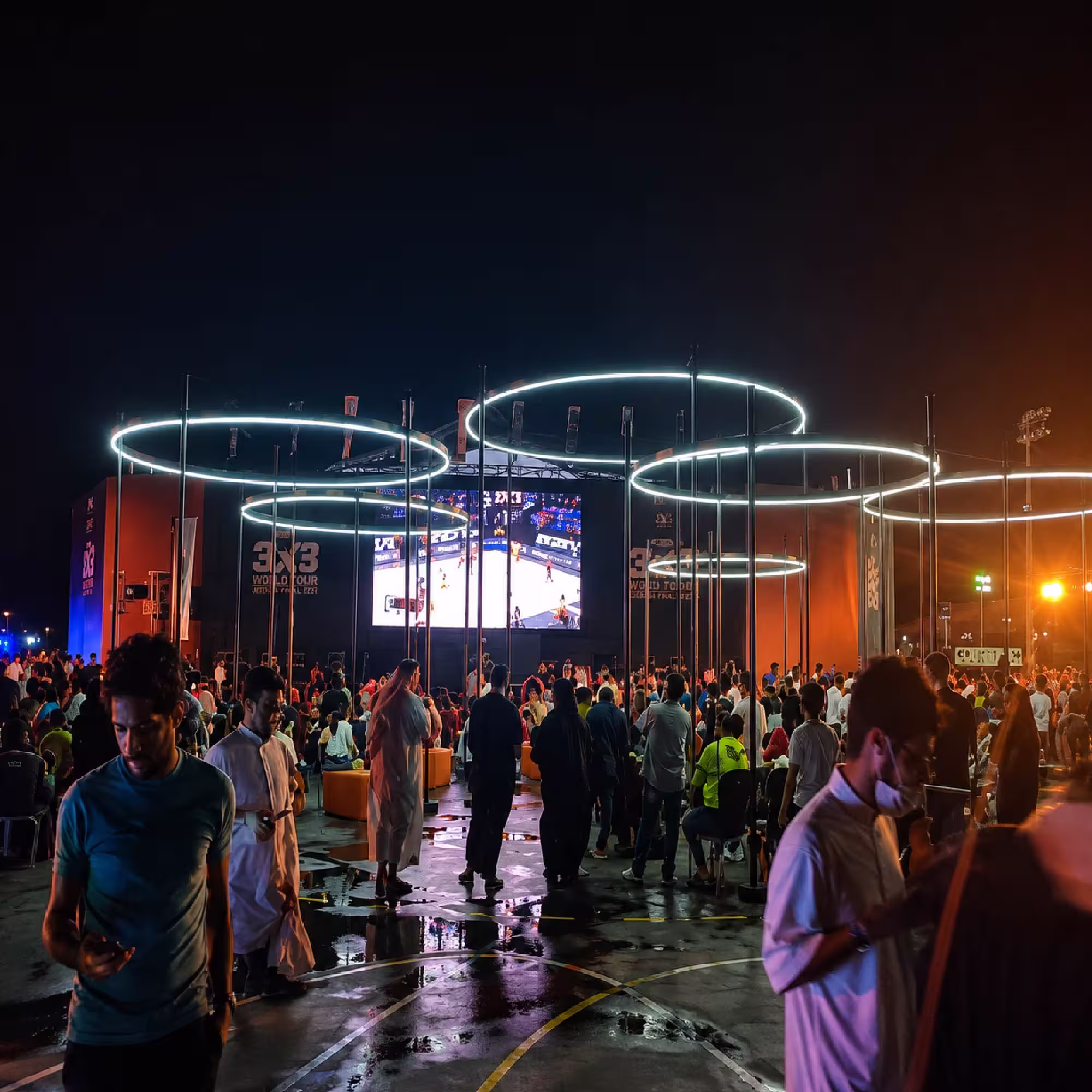 Nighttime outdoor sports event with illuminated structures, large video screen and crowd in Jeddah