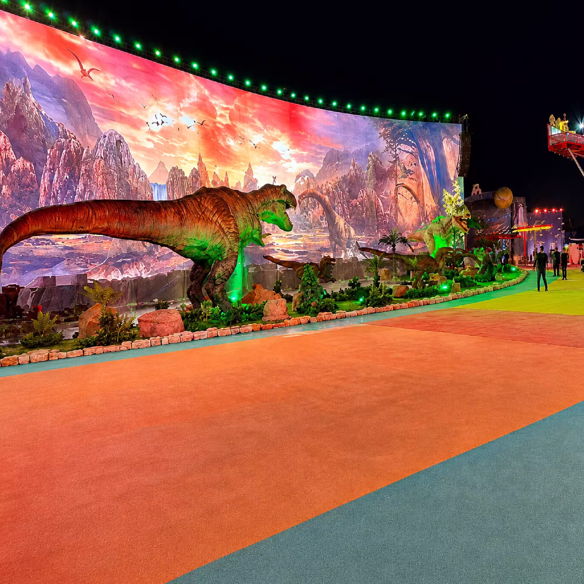Dinosaur-themed outdoor event installation with illuminated backdrop and decorative structures