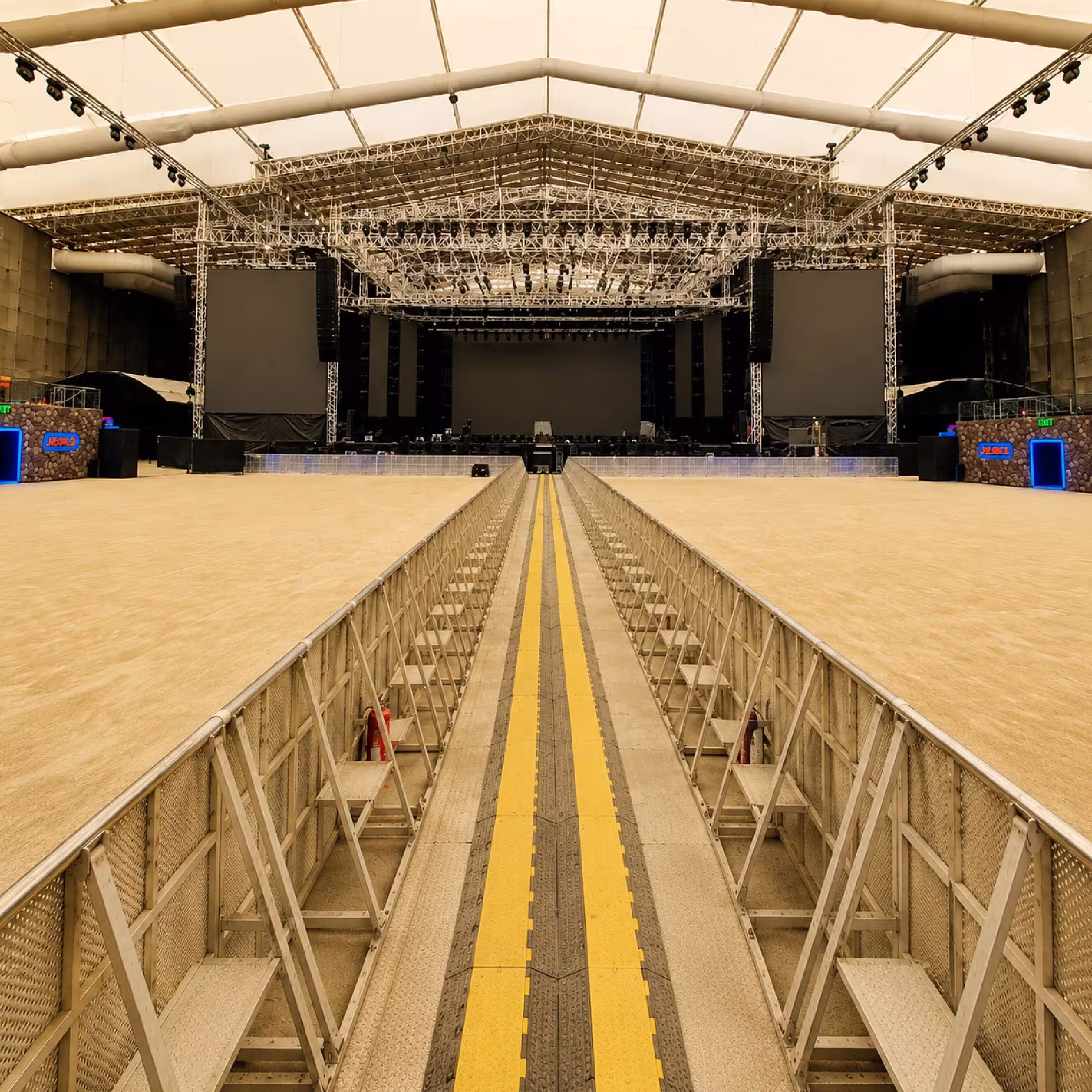 Large indoor event stage with extensive lighting truss, LED screens and audience barriers
