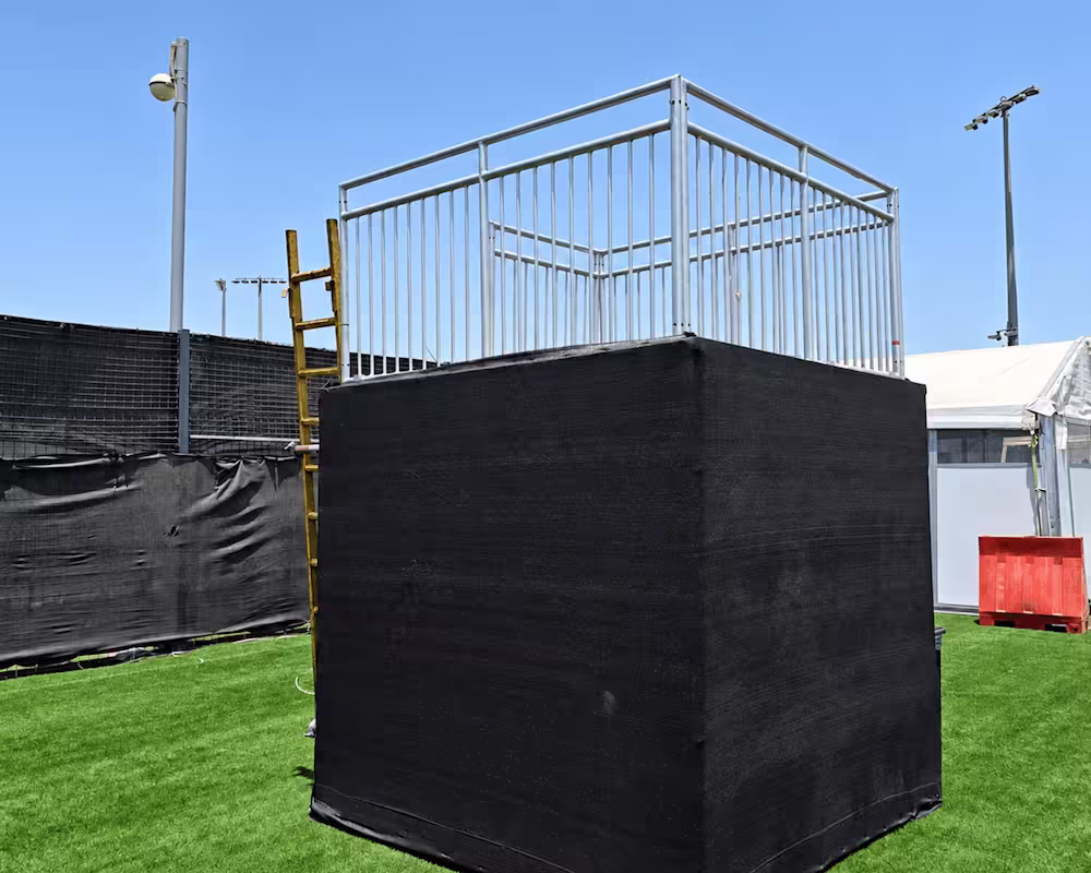 Black mesh-covered temporary scaffolding structure with metal safety railings on an outdoor event site.
