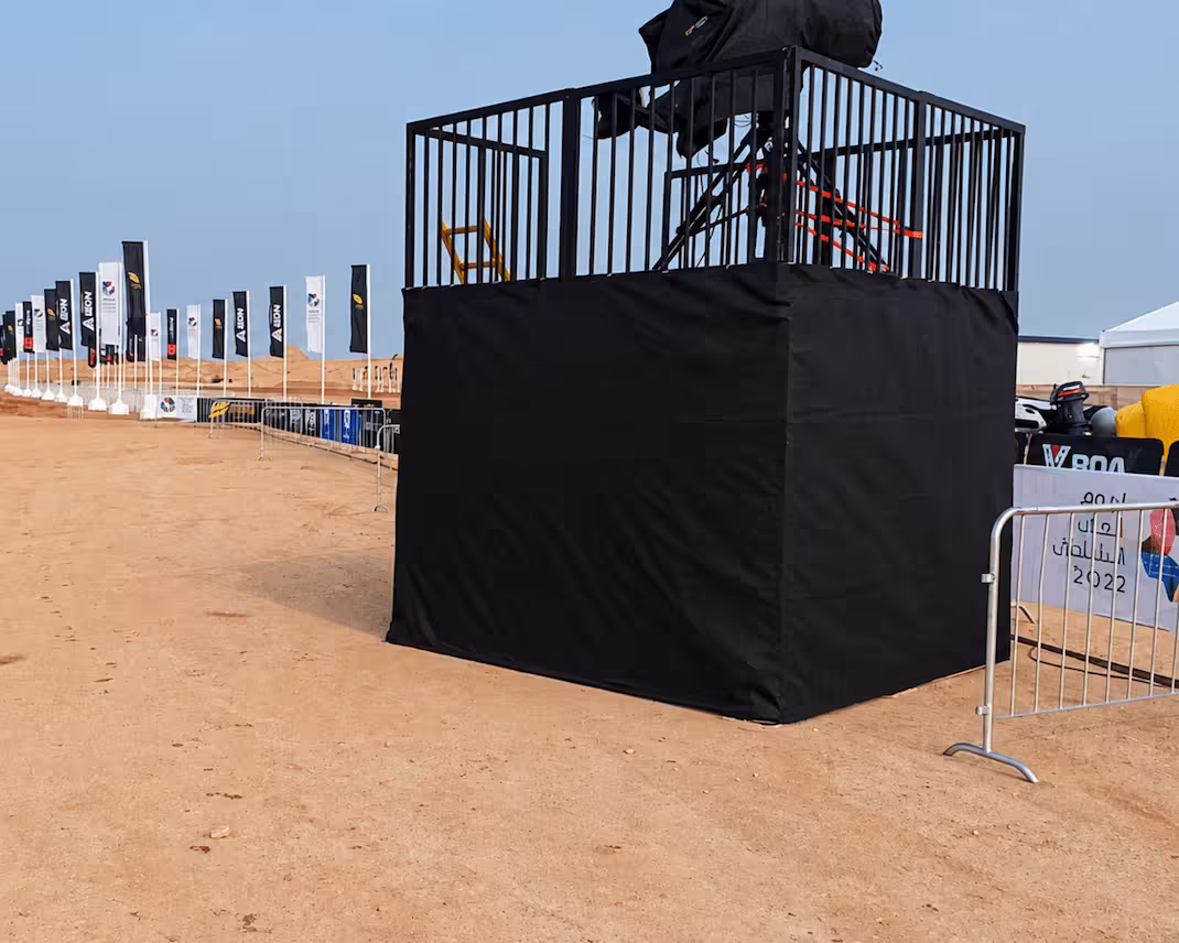 Black mesh-covered scaffolding platform with safety railings at an outdoor motorsport event.