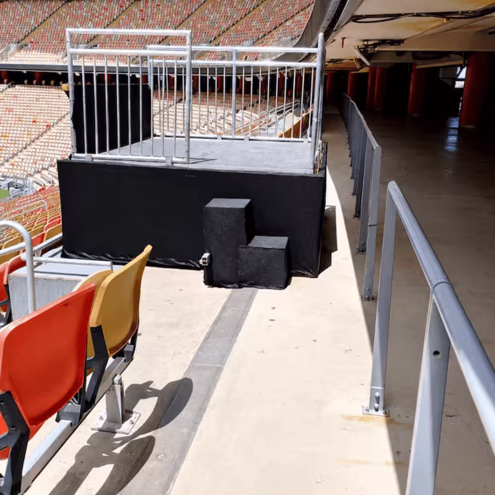 Temporary event platform with safety railings and black protective covering inside a stadium seating area.
