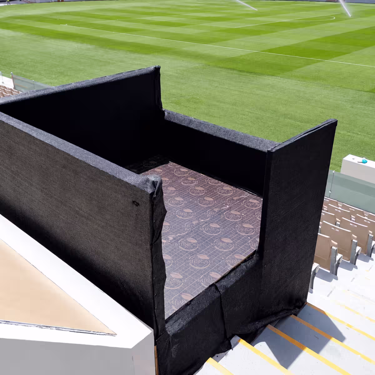 Black temporary event enclosure with carpeted flooring overlooking a football stadium.