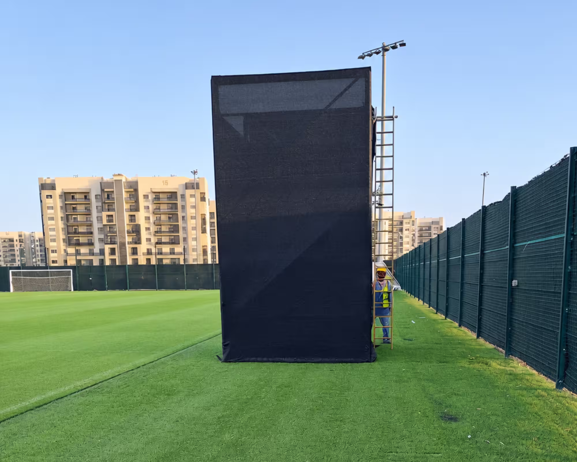 Black temporary scaffolding structure with ladder on an outdoor football field.