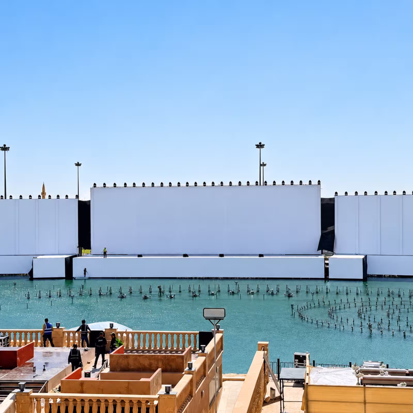 Large temporary event stage with white backdrop panels, lighting fixtures, and a water feature in the foreground.