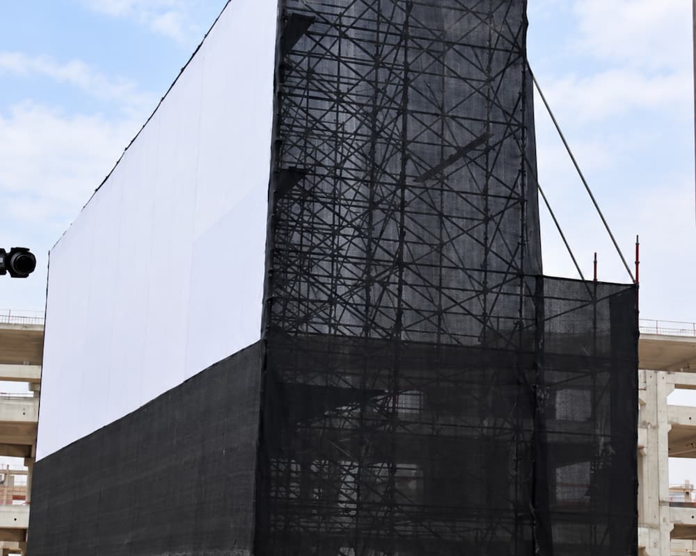 Large temporary event scaffolding structure with black mesh covering and a white screen backdrop.