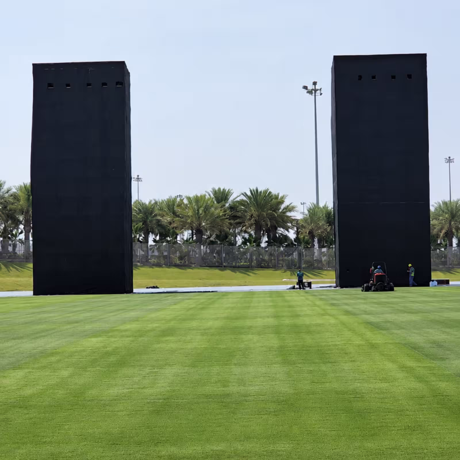 Temporary black-covered event structures with tall towers arranged across a large outdoor grass field.