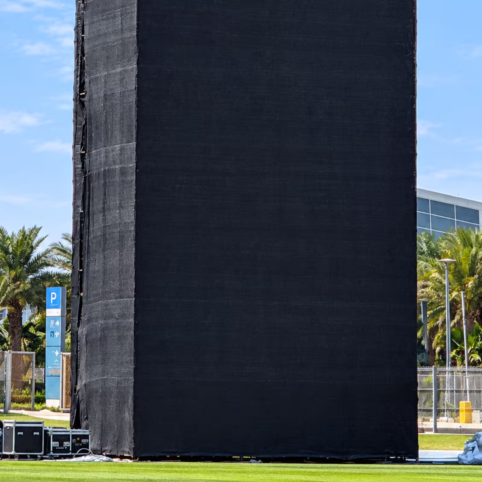 Large black mesh-covered temporary event structure on a grass field, with equipment cases beside it.