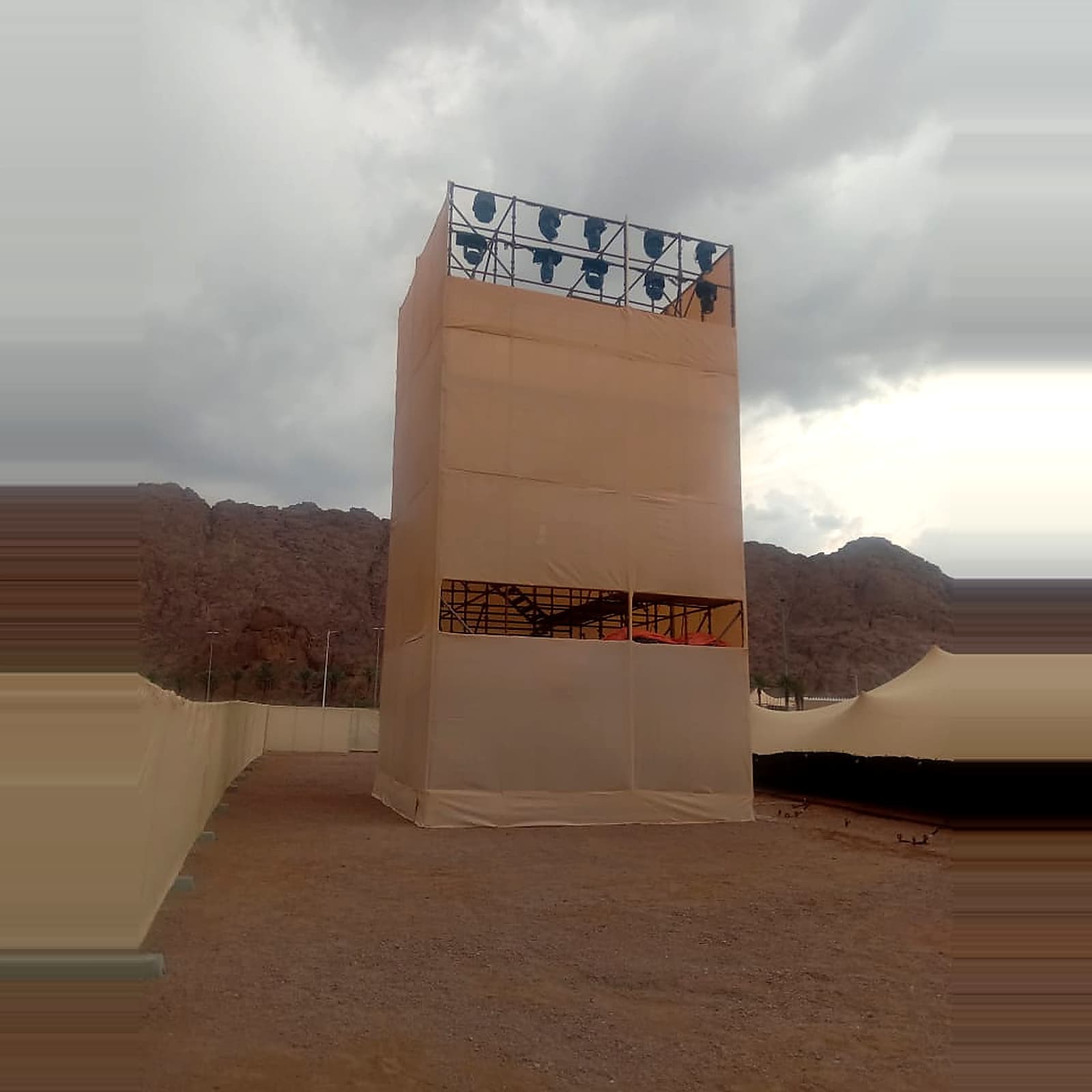 Temporary covered event tower with stage lighting, set against a mountainous outdoor venue.