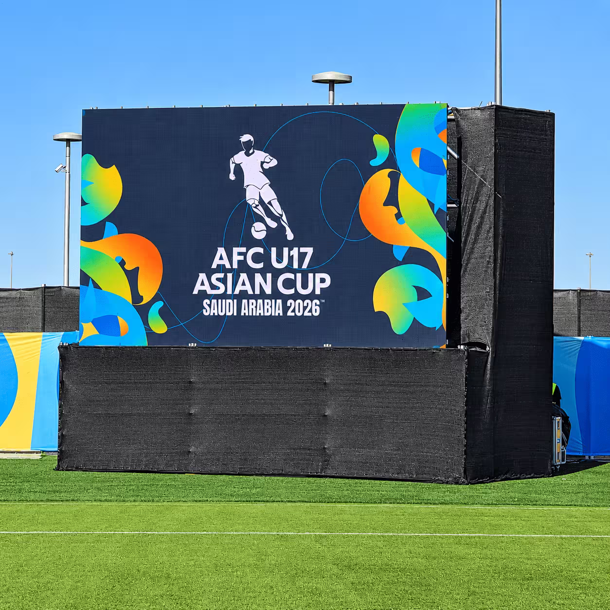Temporary event structure with a large AFC U17 Asian Cup Saudi Arabia 2026 display, black mesh covering, and sports-field setup.