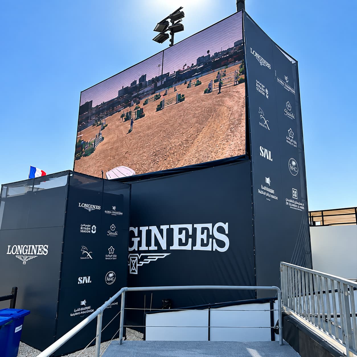 Large LONGINES-branded event display structure with a giant LED screen showing an outdoor equestrian competition.