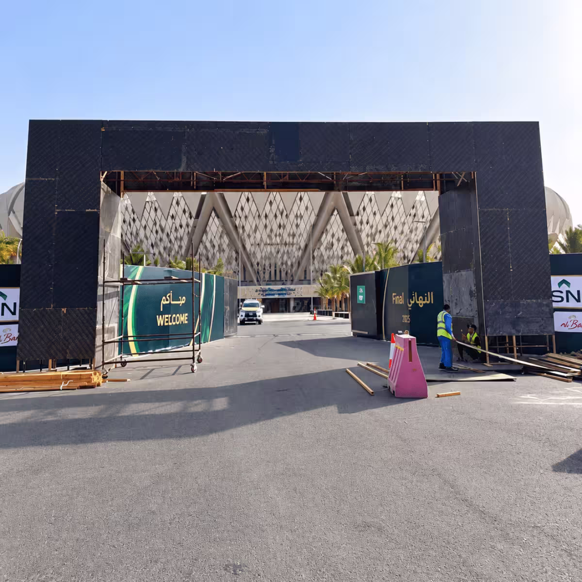 Large temporary event entrance structure with scaffolding, welcome signage, and workers preparing the venue.