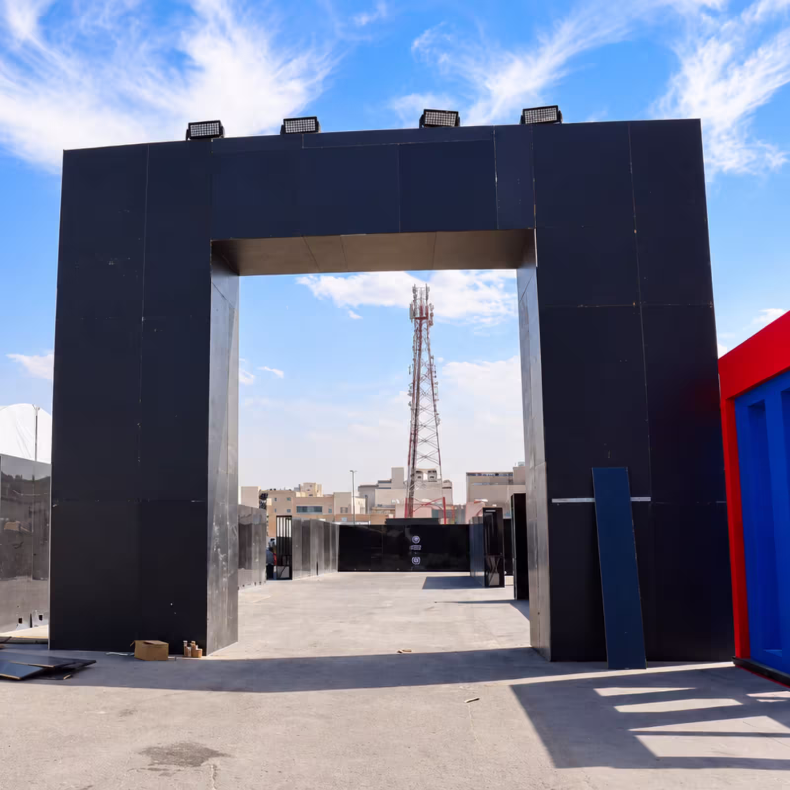 Large black temporary event entrance with overhead lighting, set against a clear blue sky and urban backdrop.