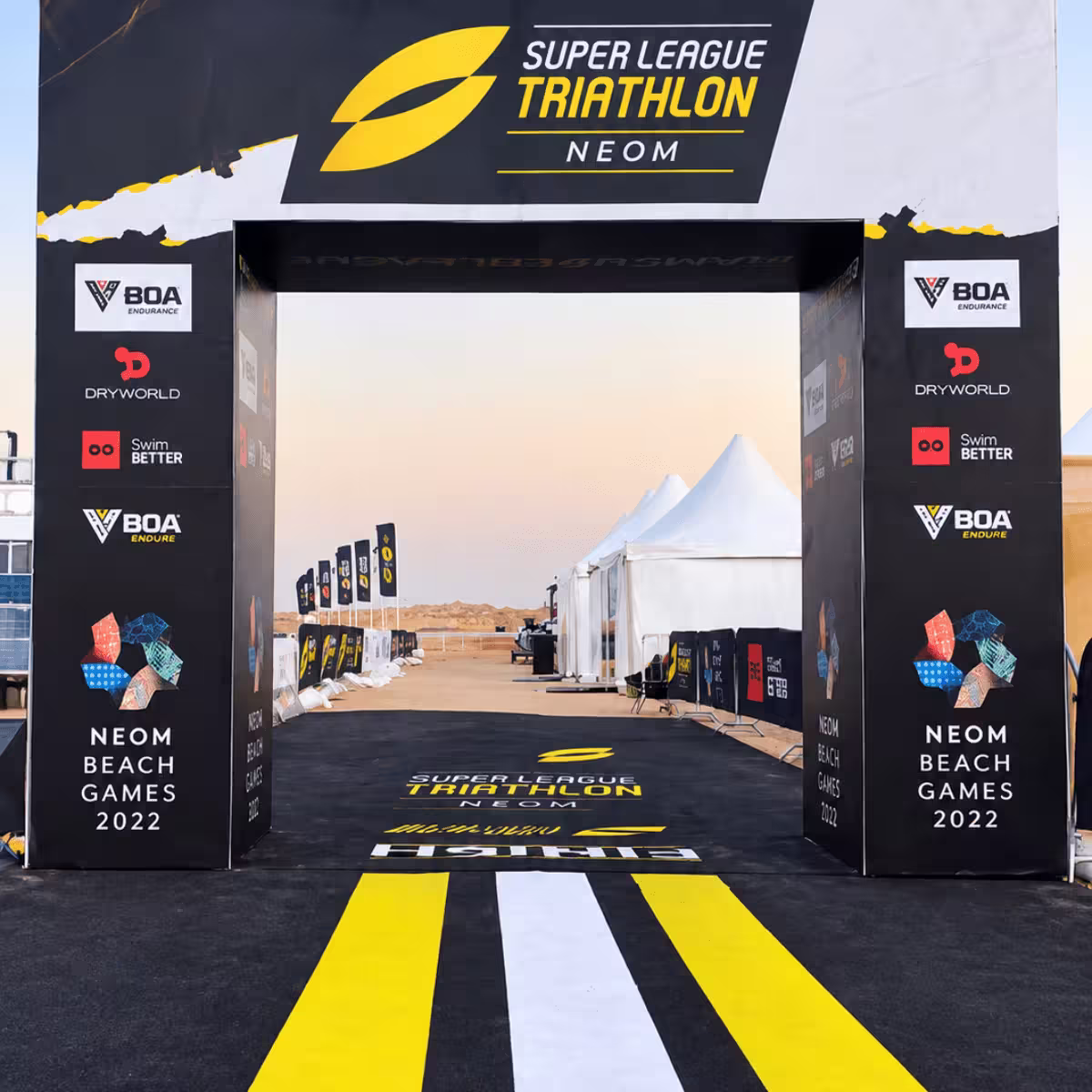 Super League Triathlon NEOM event entrance arch with branded signage and a desert event venue in the background.