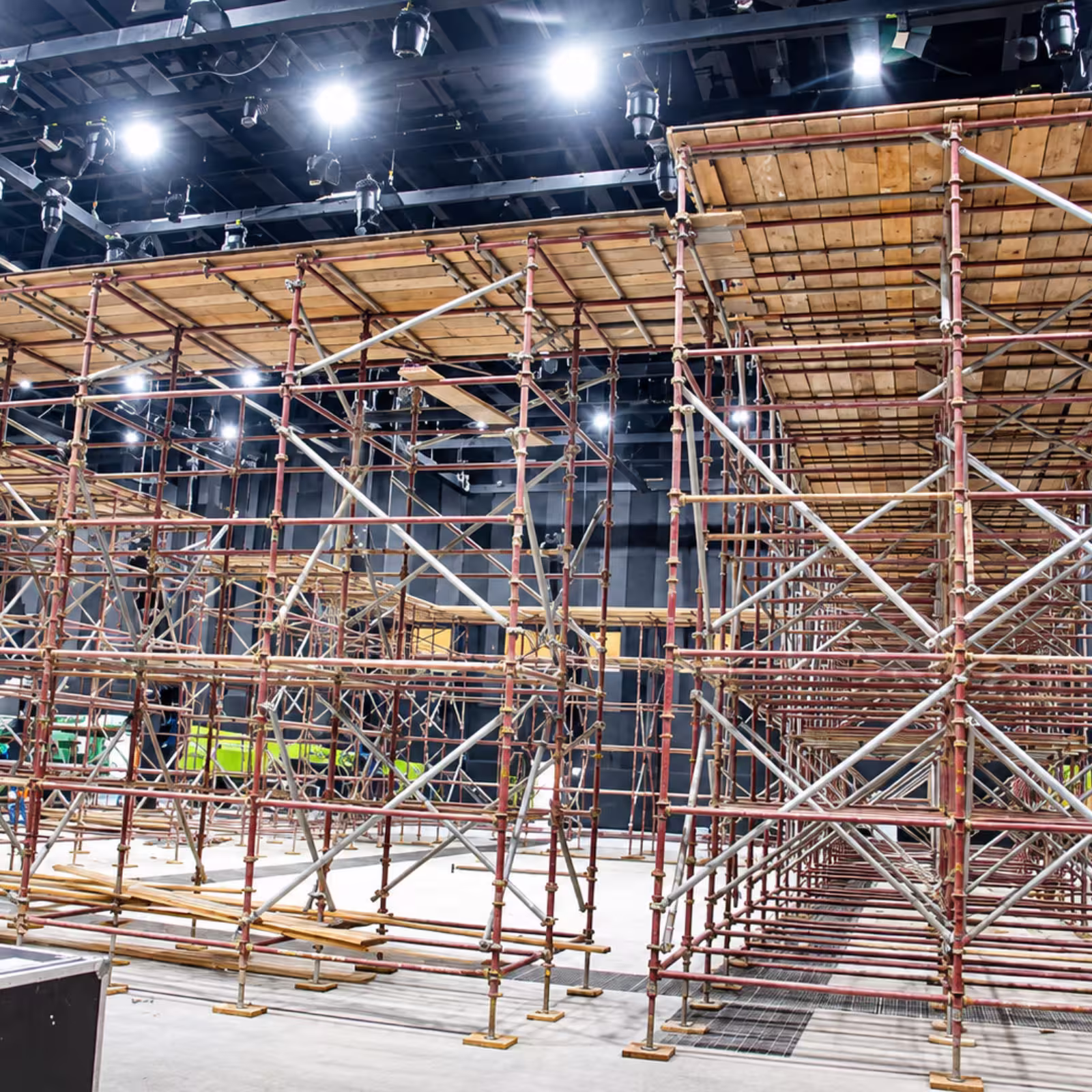 Indoor event venue with extensive metal scaffolding supporting multi-level wooden platforms and overhead stage lighting.