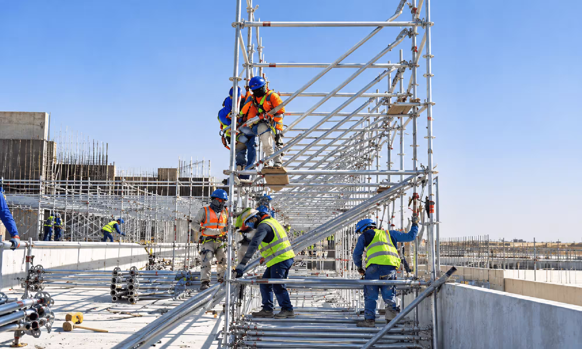 Workers installing ring lock scaffolding on a large construction site using metal frames, platforms, and safety equipment.
