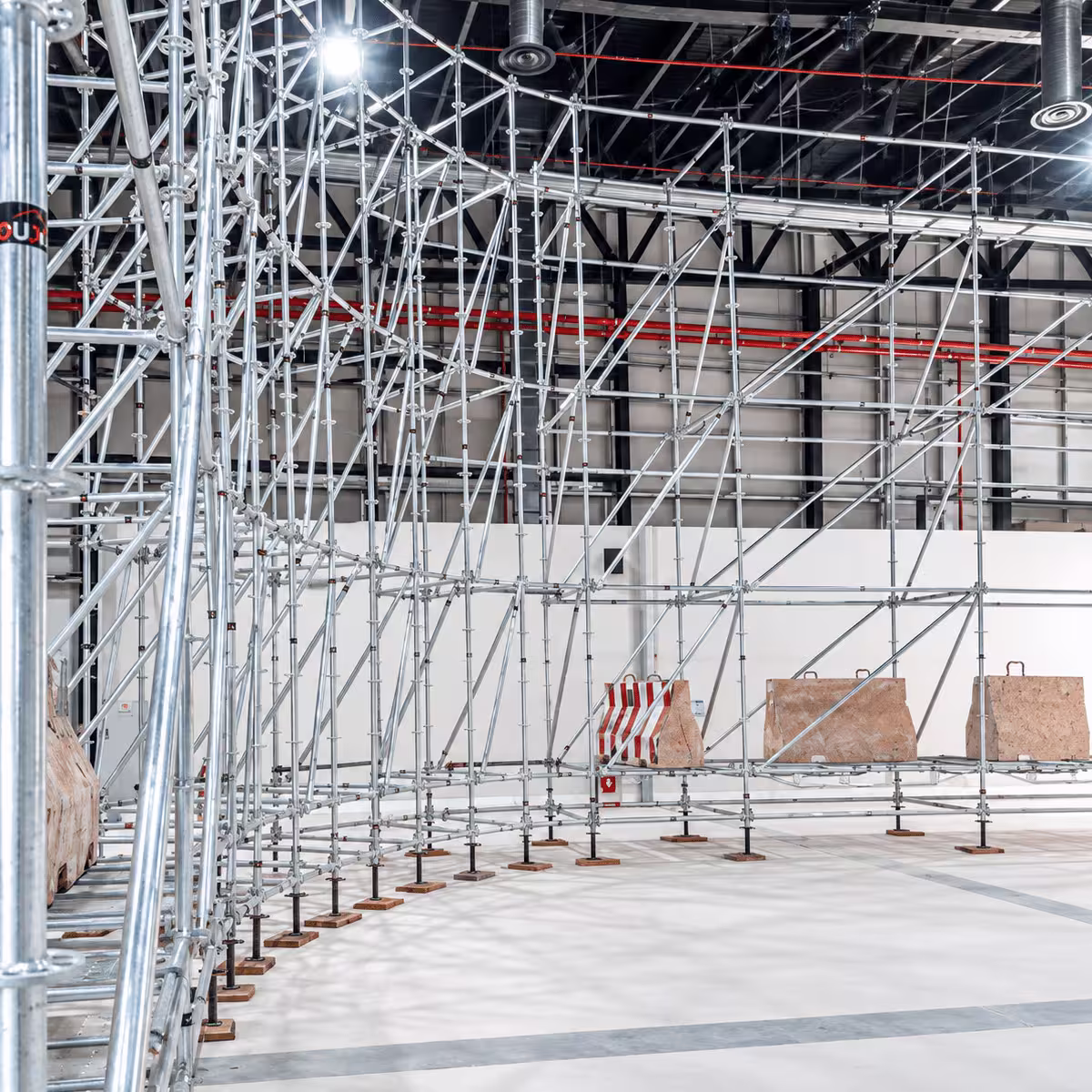 Indoor ring lock scaffolding system installed inside a large industrial facility with metal frames, diagonal braces, and support platforms.
